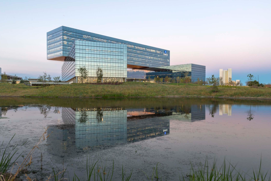 Zurich North America headquarters at 90 North Schaumburg, reflecting in a tranquil pond and surrounded by lush natural landscapes.